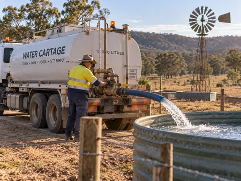 Water carter filling a rural water tank from a tanker truck